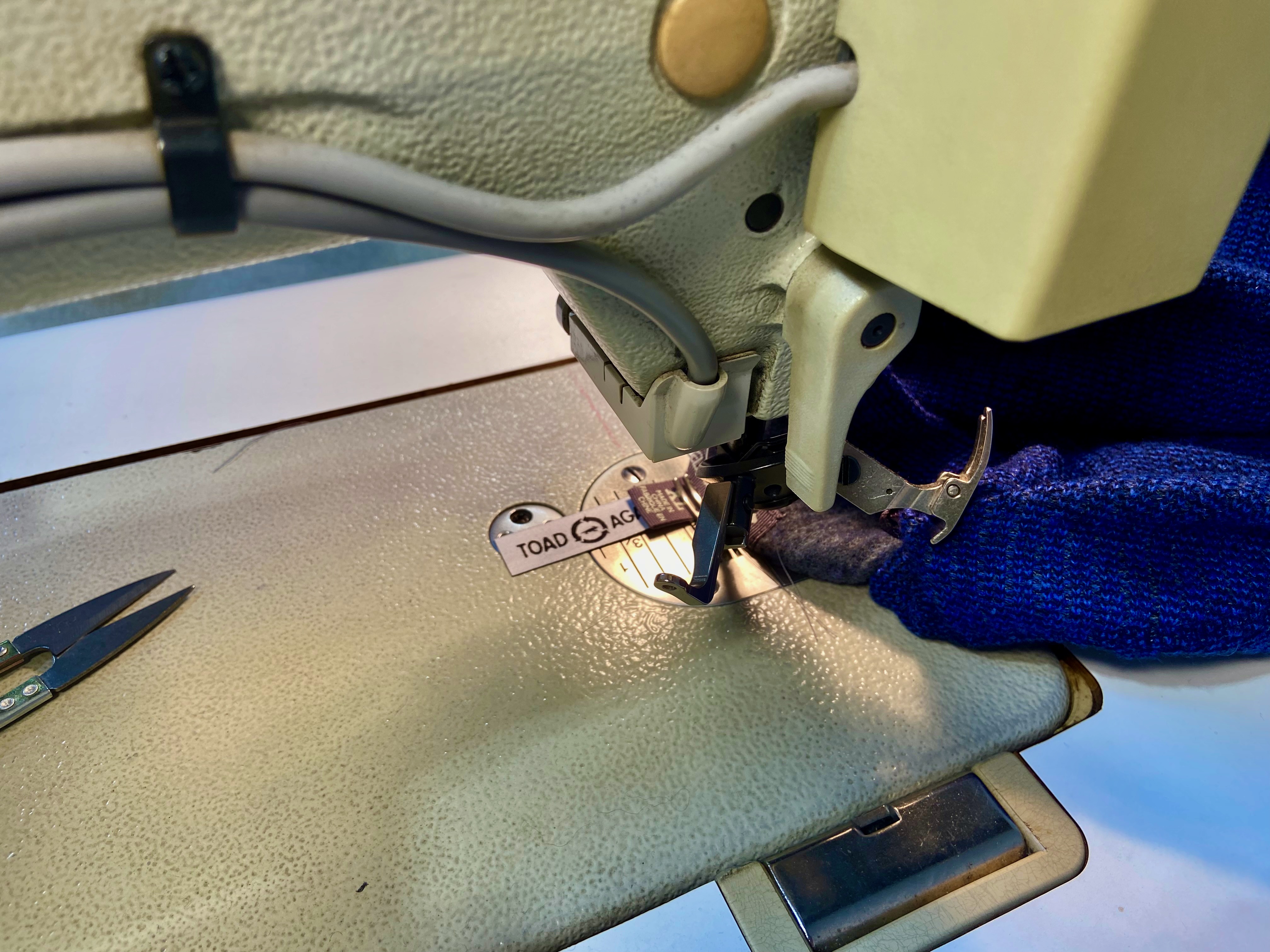 A closeup of a sewing machine used to attach a tag to a garment.