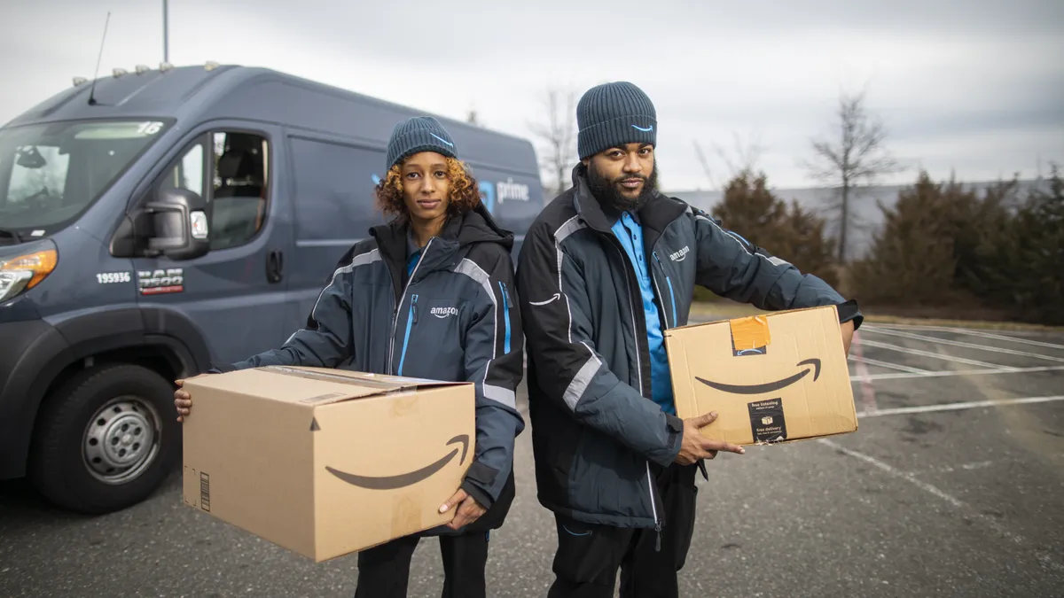 Two people wearing knit hats and company jackets holding packages.