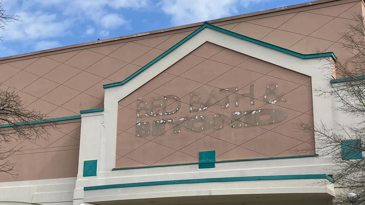 A Bed Bath & Beyond label scar is seen on a beige storefront with a blue sky.