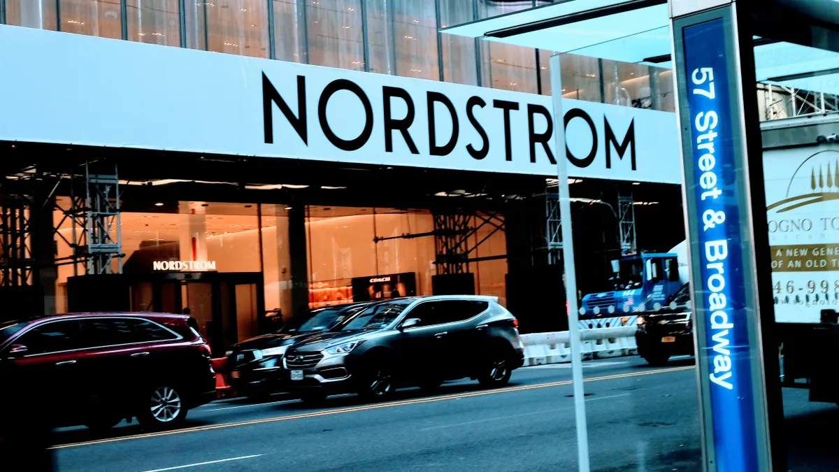 A bus stop with a bright blue sign that reads "57th Street and Broadway" sits across the street from a Nordstrom store.