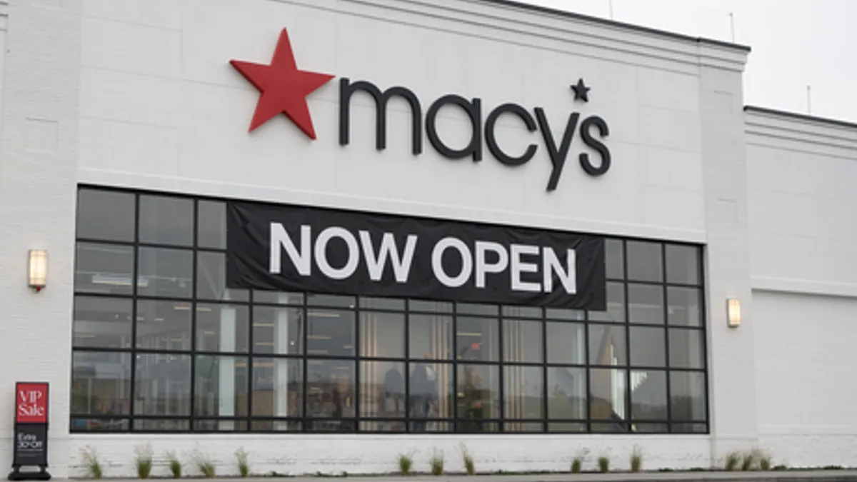 A white store with a Macy's banner and red store, with a "Now Open" sign on the windows.