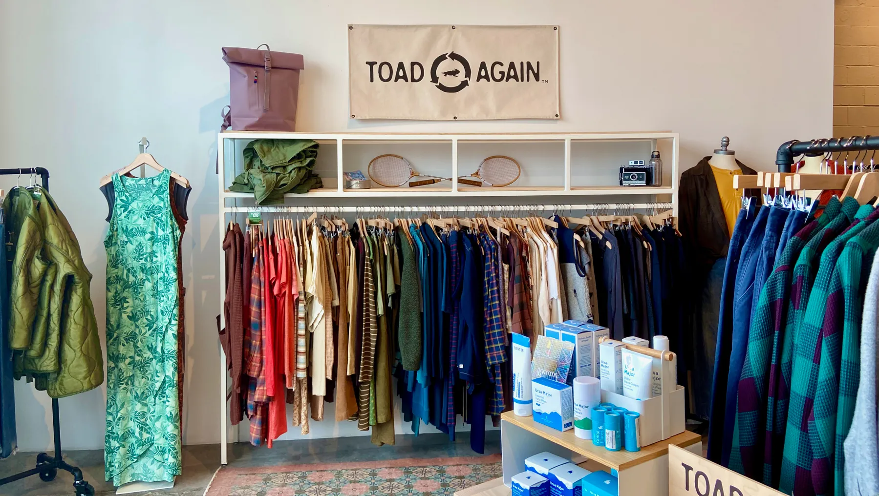 The inside of an apparel store, with clothes hanging on a rack underneath a sign that reads "Toad Again."