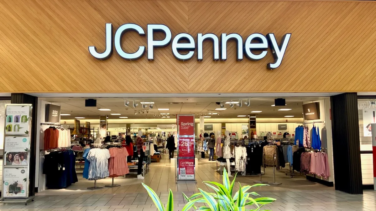 The interior entrance to a JC Penney mall store, with fronds of a plant in the foreground.