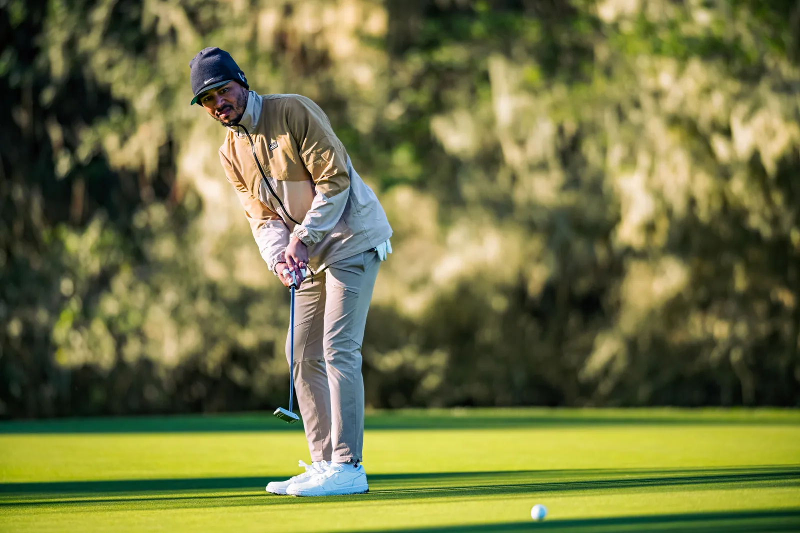 Baseball player Mookie Betts wears an outfit by Blackballed Golf as he swings his golf club on the green.